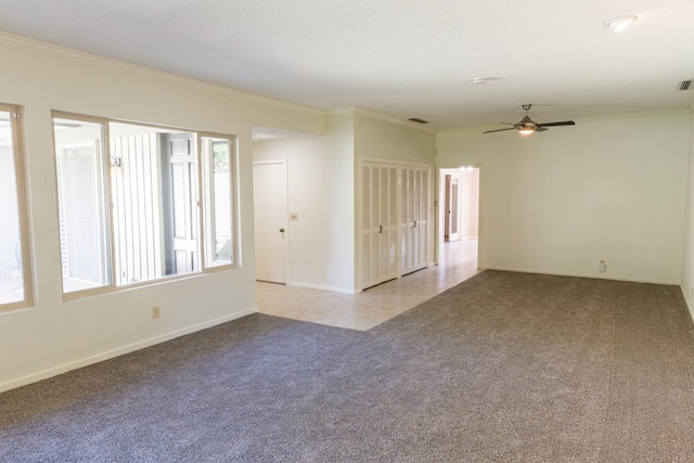 carpeted empty room featuring baseboards, visible vents, a ceiling fan, and crown molding