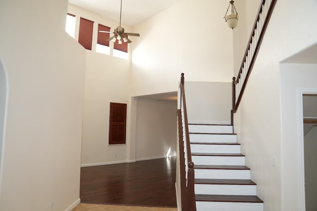 staircase with ceiling fan, hardwood / wood-style floors, and a high ceiling