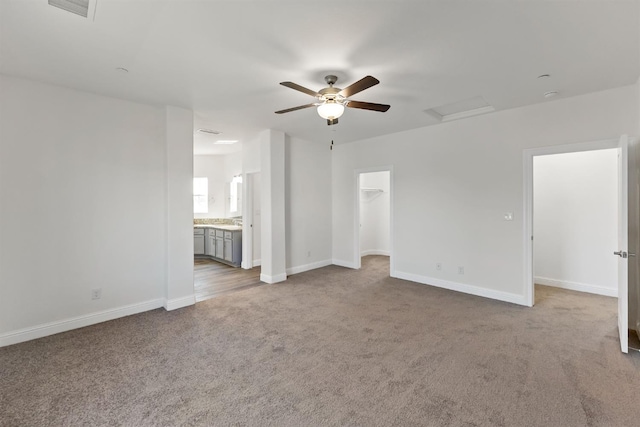 interior space with light carpet, ensuite bath, ceiling fan, and a walk in closet