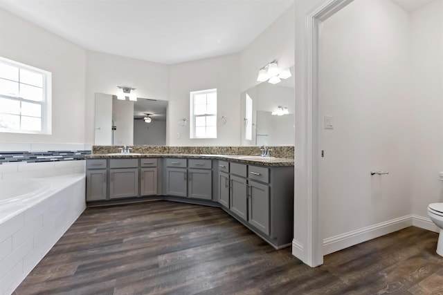 bathroom featuring a relaxing tiled tub, vanity, hardwood / wood-style floors, and toilet