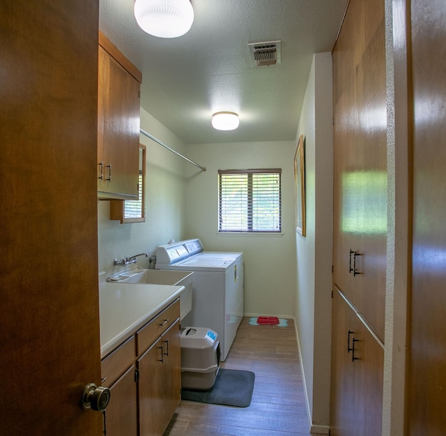 washroom featuring a textured ceiling, light hardwood / wood-style flooring, cabinets, sink, and washing machine and clothes dryer