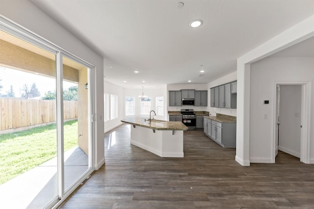 kitchen featuring gray cabinetry, dark wood-type flooring, an island with sink, a breakfast bar, and appliances with stainless steel finishes