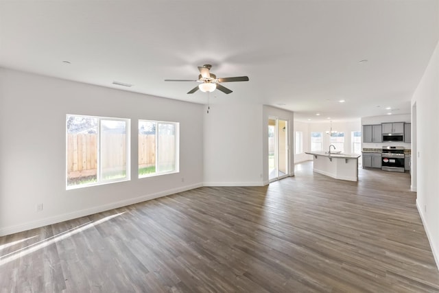 unfurnished living room with sink, ceiling fan with notable chandelier, and dark hardwood / wood-style floors