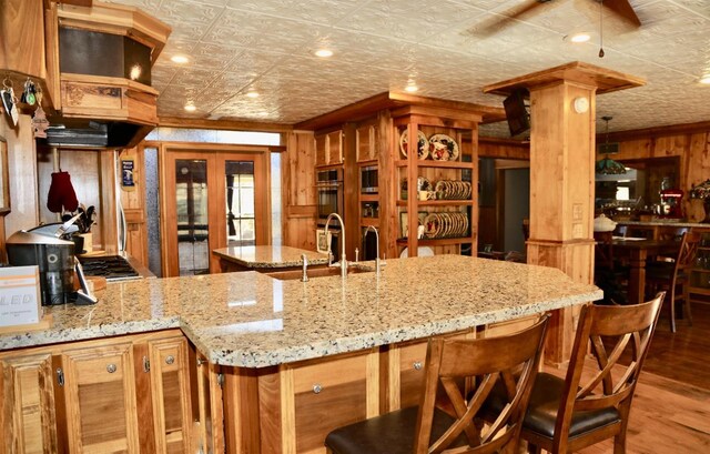 kitchen featuring a sink, an ornate ceiling, wood finished floors, wood walls, and light stone counters