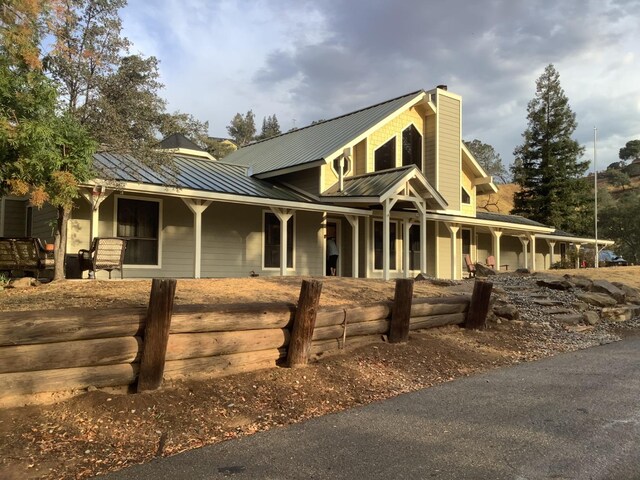 view of front facade featuring metal roof, a chimney, a standing seam roof, and covered porch