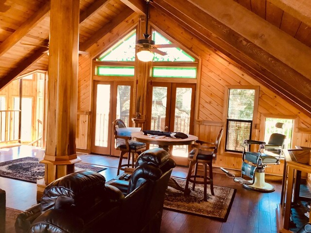living room with ceiling fan, wood walls, hardwood / wood-style flooring, and lofted ceiling with beams