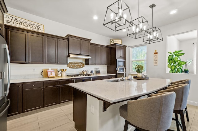 kitchen featuring appliances with stainless steel finishes, an inviting chandelier, decorative light fixtures, a center island with sink, and sink