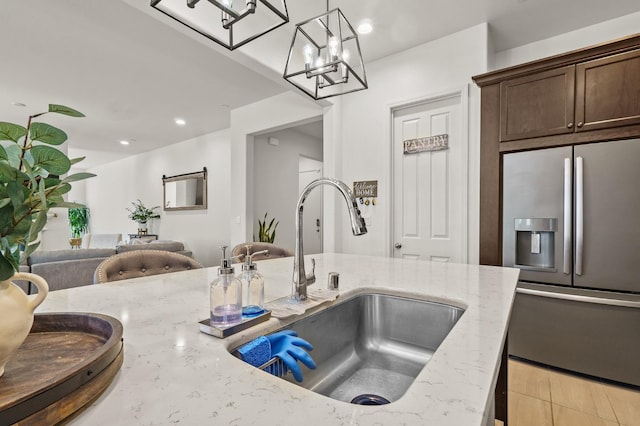 kitchen with stainless steel fridge with ice dispenser, sink, a notable chandelier, decorative light fixtures, and light stone countertops