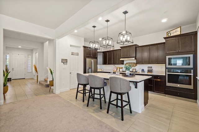 kitchen featuring a chandelier, a kitchen island with sink, hanging light fixtures, stainless steel appliances, and dark brown cabinetry