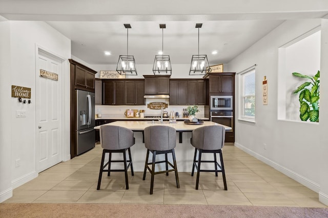 kitchen with appliances with stainless steel finishes, a kitchen island with sink, dark brown cabinets, and pendant lighting