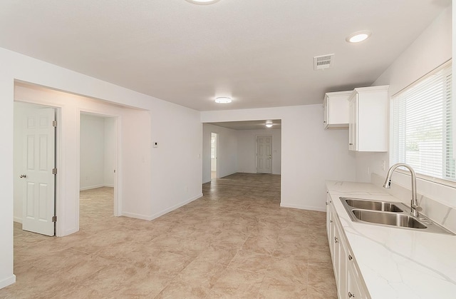 kitchen featuring light stone countertops, white cabinetry, and sink