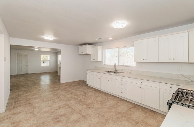 kitchen with light stone counters, white cabinets, sink, and a wealth of natural light