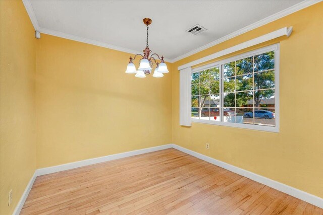 spare room featuring wood-type flooring, ornamental molding, and an inviting chandelier