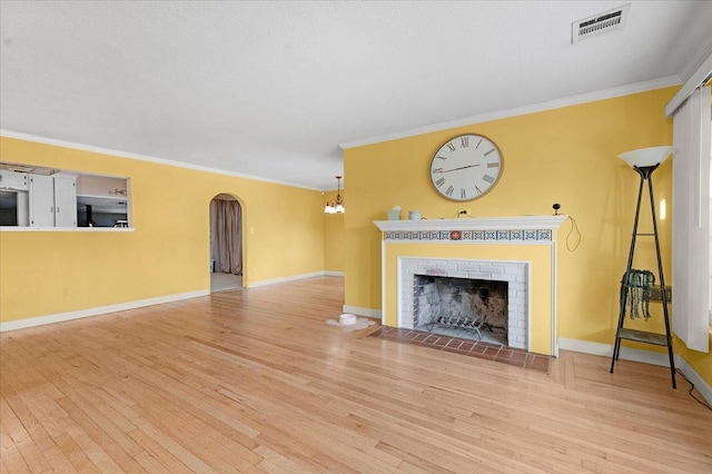 unfurnished living room with a chandelier, light hardwood / wood-style floors, a brick fireplace, and crown molding