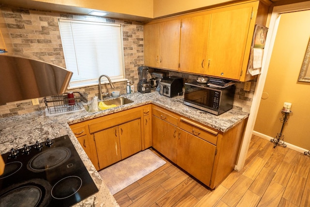 kitchen featuring light stone counters, sink, tasteful backsplash, light hardwood / wood-style flooring, and black electric stovetop