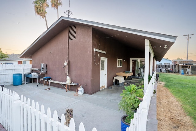 back house at dusk featuring a yard and a patio area