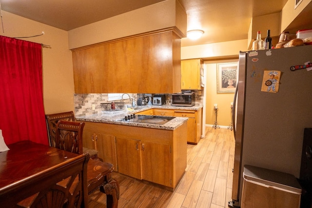 kitchen with light hardwood / wood-style flooring, stainless steel appliances, kitchen peninsula, and tasteful backsplash