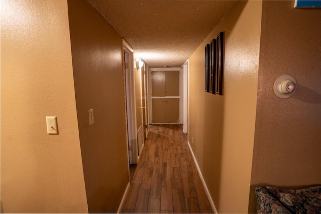 corridor with a textured ceiling and wood-type flooring