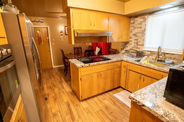 kitchen with light wood-type flooring, kitchen peninsula, decorative backsplash, appliances with stainless steel finishes, and light stone countertops