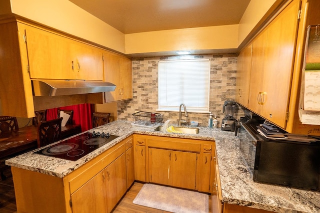 kitchen featuring light wood-type flooring, sink, kitchen peninsula, backsplash, and black electric cooktop