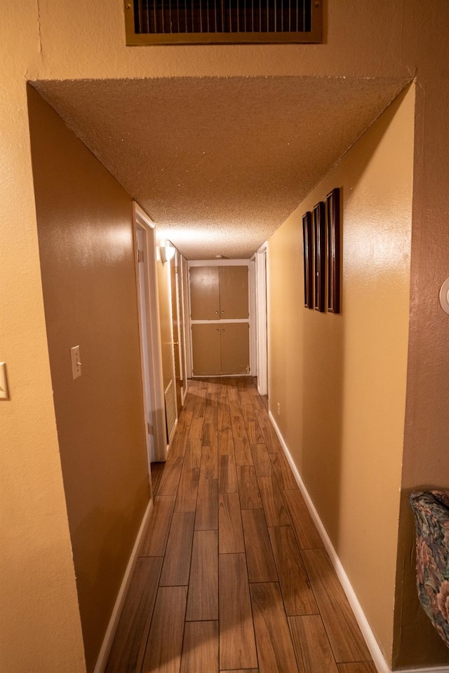 hallway with a textured ceiling and hardwood / wood-style flooring