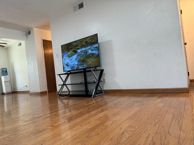 living room with ceiling fan, a textured ceiling, and light hardwood / wood-style flooring