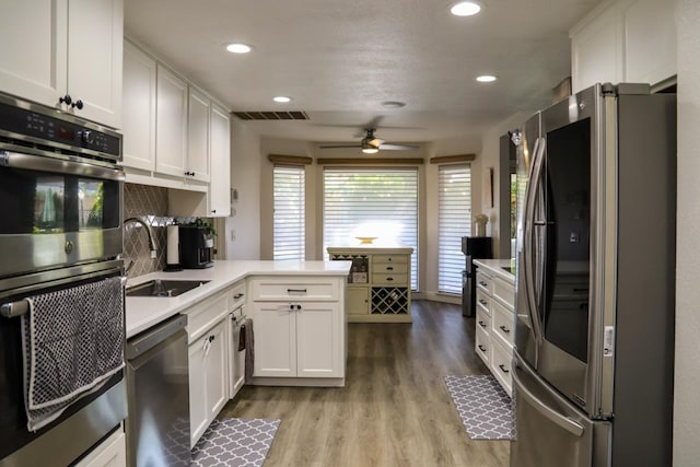 kitchen with light wood-type flooring, sink, white cabinetry, kitchen peninsula, and stainless steel appliances