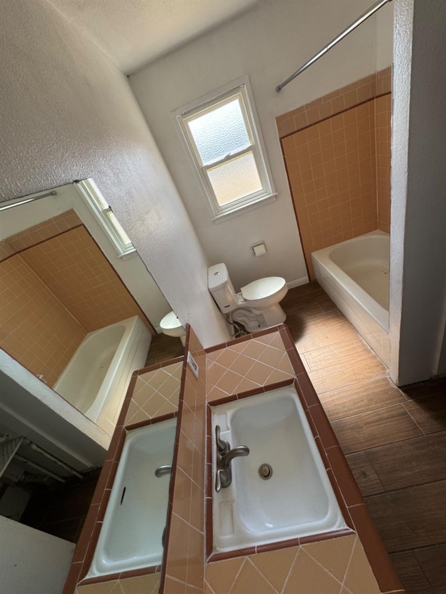 bathroom with hardwood / wood-style flooring, tiled shower / bath, and toilet