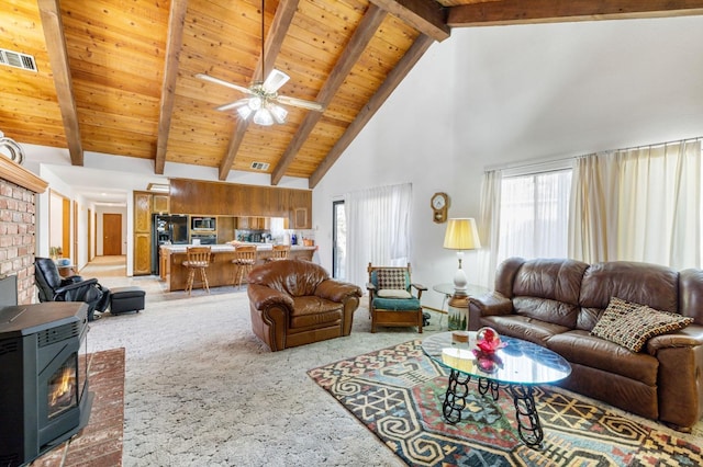 living room featuring ceiling fan, beamed ceiling, carpet flooring, a wood stove, and high vaulted ceiling