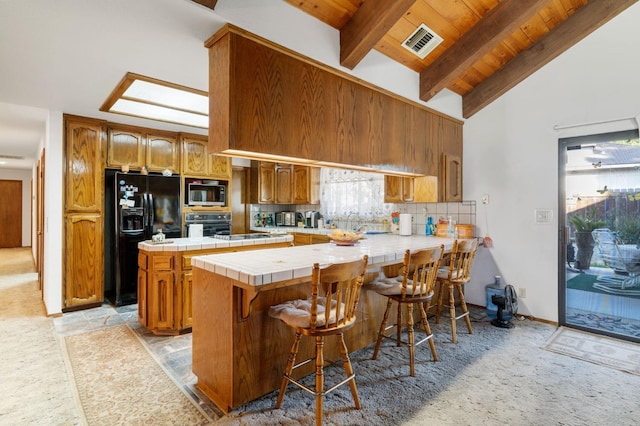 kitchen featuring wood ceiling, tile counters, beamed ceiling, kitchen peninsula, and black appliances