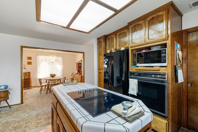 kitchen with a notable chandelier, black appliances, and tile countertops