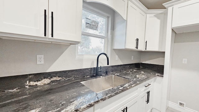 kitchen with dark stone counters, white cabinets, and sink