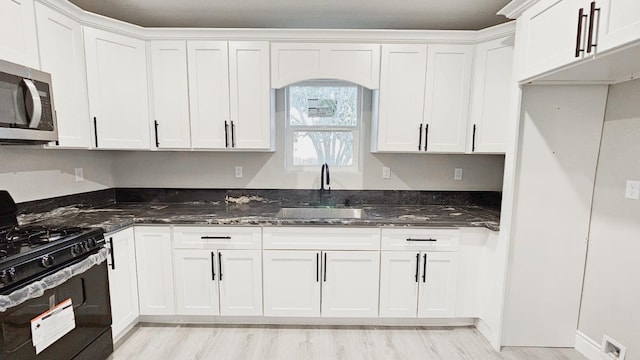 kitchen with dark stone countertops, black gas range oven, sink, and white cabinets