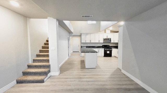 kitchen with light wood-type flooring, black stove, and white cabinets