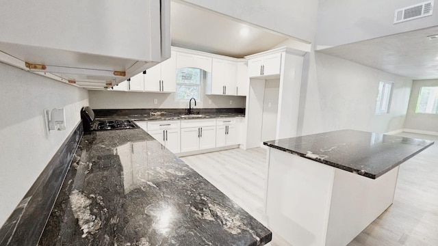 kitchen with dark stone countertops, white cabinets, sink, and a healthy amount of sunlight