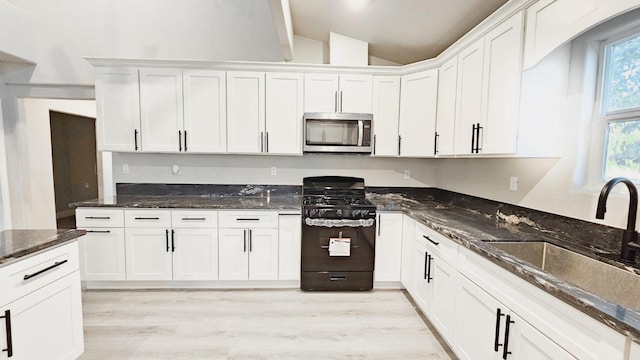 kitchen with white cabinets, sink, black range with gas cooktop, light wood-type flooring, and vaulted ceiling