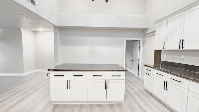 kitchen with dark stone countertops, light wood-type flooring, and white cabinetry