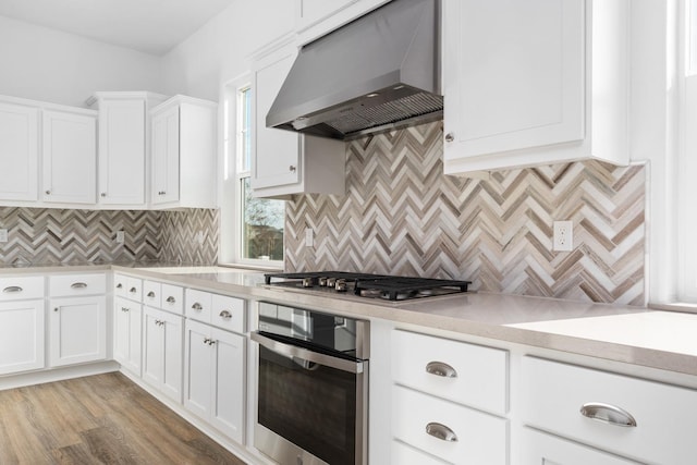 kitchen featuring under cabinet range hood, stainless steel appliances, white cabinets, light countertops, and decorative backsplash