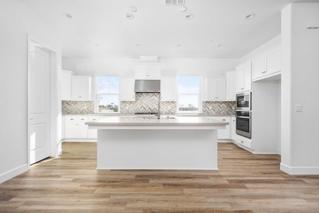 kitchen featuring appliances with stainless steel finishes, a kitchen island with sink, plenty of natural light, and wall chimney exhaust hood