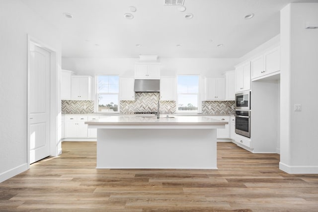 kitchen with appliances with stainless steel finishes, light wood-type flooring, white cabinets, and under cabinet range hood