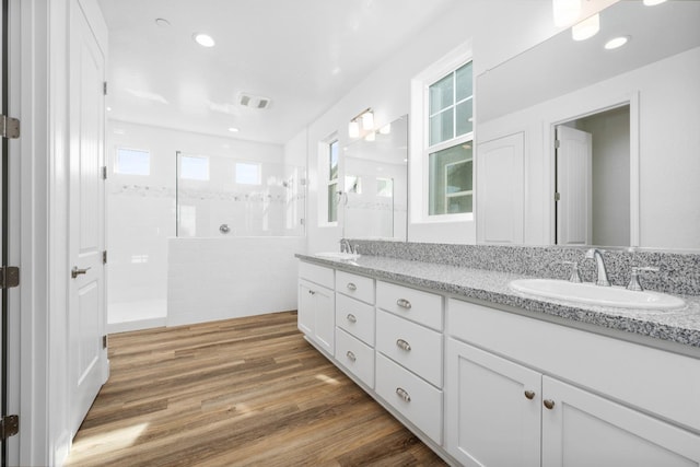 full bath featuring double vanity, walk in shower, a sink, and wood finished floors