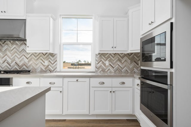 kitchen with tasteful backsplash, appliances with stainless steel finishes, light countertops, wall chimney range hood, and white cabinetry