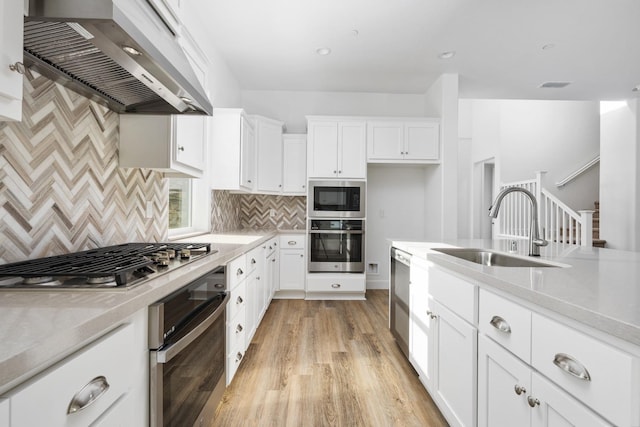 kitchen with a sink, light countertops, appliances with stainless steel finishes, wall chimney exhaust hood, and light wood finished floors