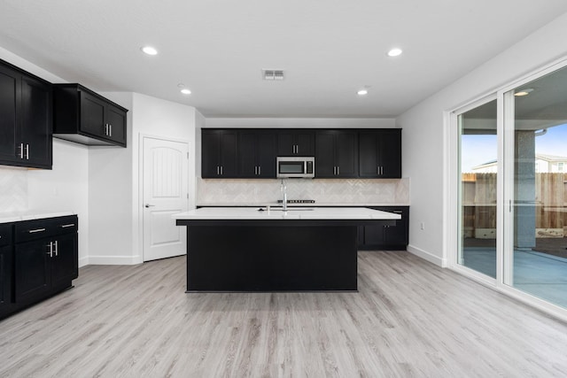 kitchen featuring stainless steel microwave, backsplash, visible vents, light countertops, and dark cabinets