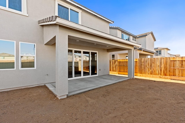 rear view of house with stucco siding, fence, and a patio