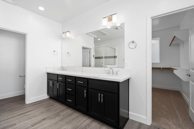 bathroom featuring a shower stall, double vanity, baseboards, and wood finished floors