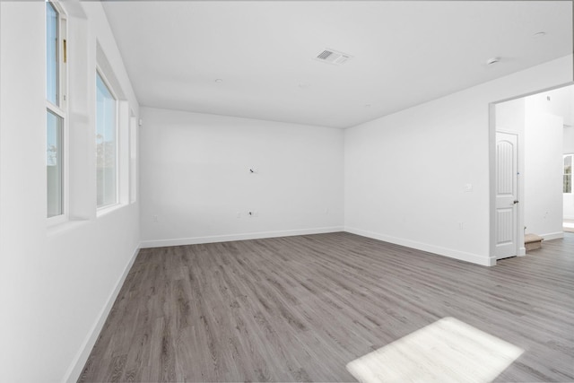 unfurnished room with healthy amount of natural light, wood finished floors, and baseboards