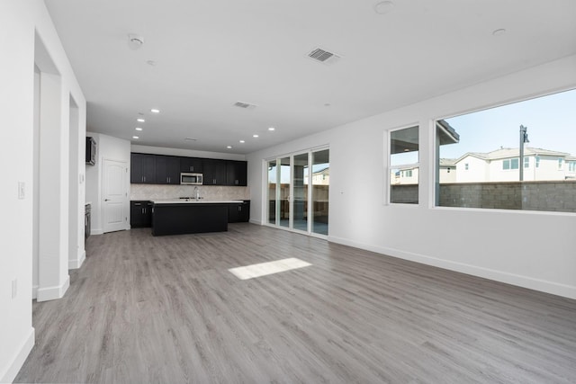 kitchen featuring stainless steel microwave, backsplash, visible vents, open floor plan, and dark cabinetry