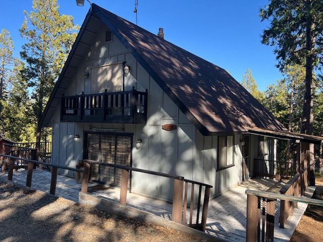 exterior space with a shingled roof, board and batten siding, a chimney, and a balcony