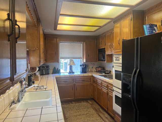 kitchen with black appliances, tile counters, backsplash, and sink